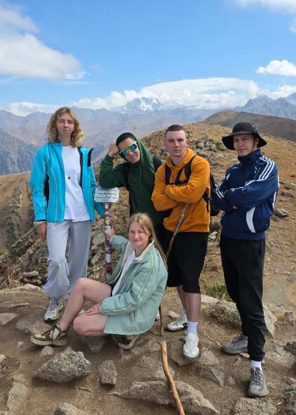 Five friends on a mountain trail under a blue sky. Kotya's signature appears on the photo as it is signed.