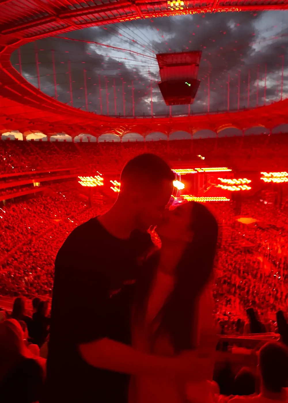 A couple kissing at a stadium concert lit in red, with Lazko Alex's signature in white ink.